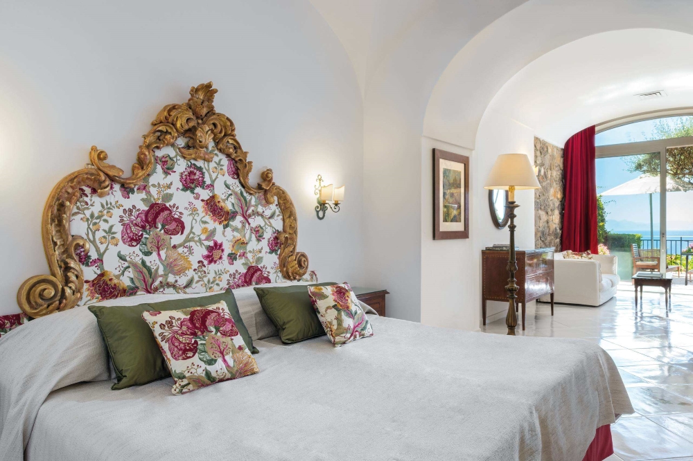 Elegant suite at Santa Caterina Hotel in Amalfi with an ornate headboard, arched ceiling and sea-view terrace